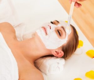 17260959 - therapist applying a face mask to the face of a beautiful young blonde woman using a cosmetic brush