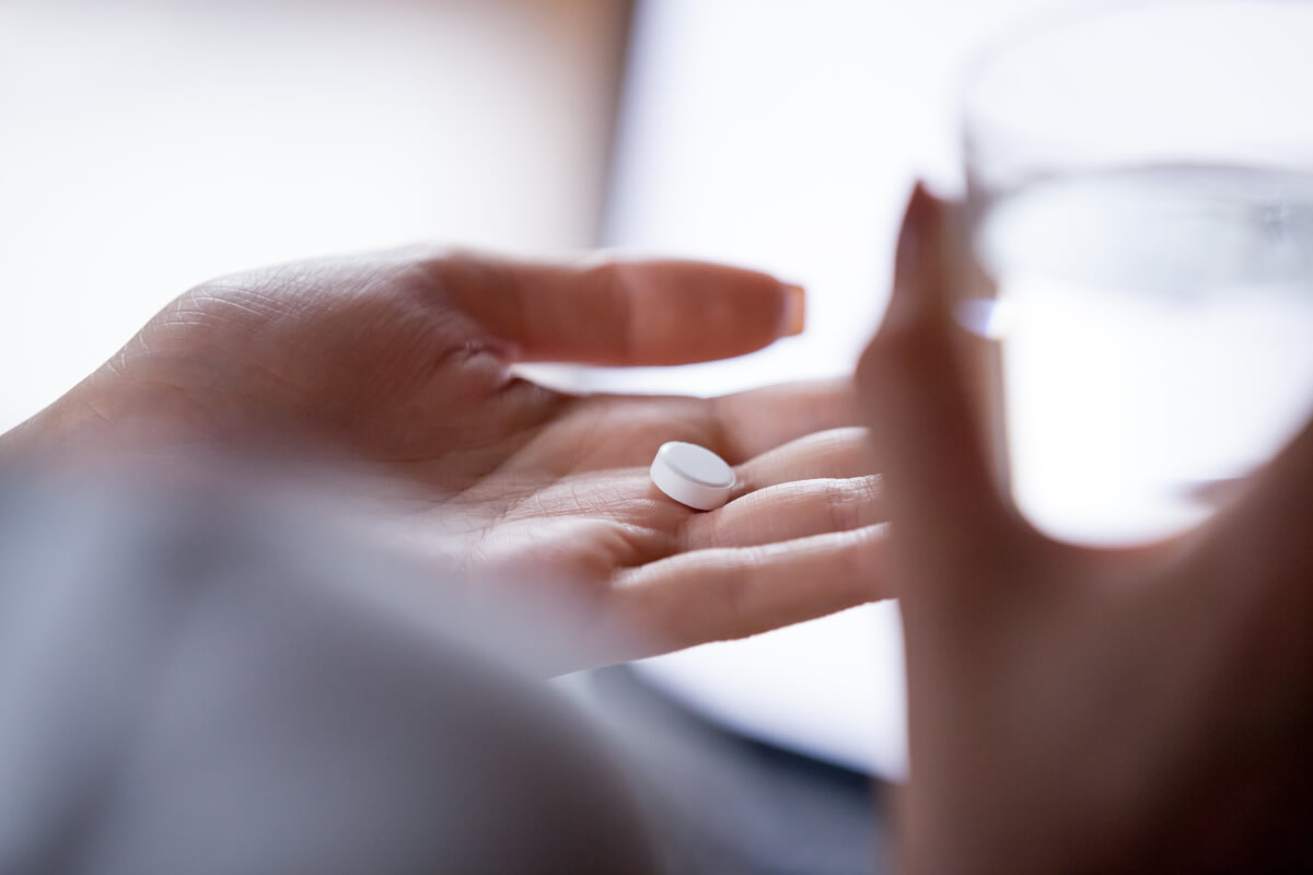 Close up woman holding pill in hand with water.