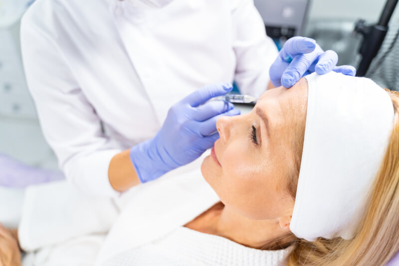 Female patient in a headband receiving a facial injection for wrinkles in a beauty clinic