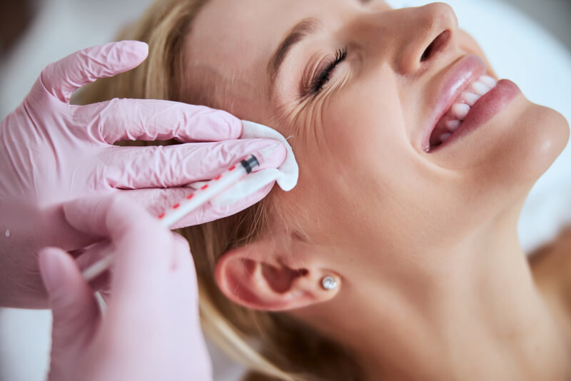 Smiling lady lying with her eyes closed during the Botox injection