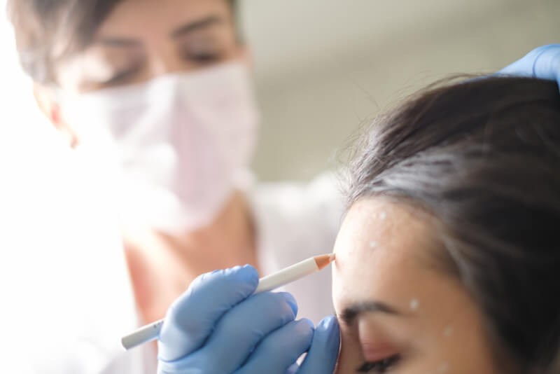Aesthetician injecting botox to woman's forehead