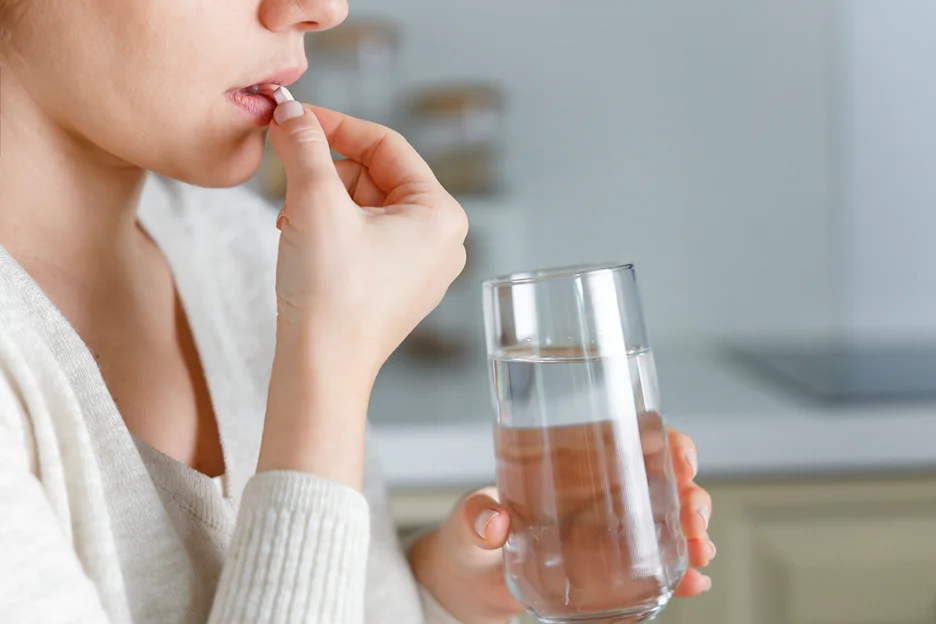 a woman taking a pill with a glass of water